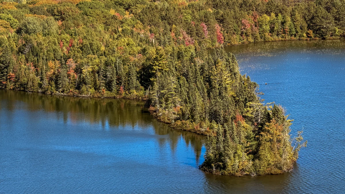Wooded peninsula surrounded by blue lake water in autumn