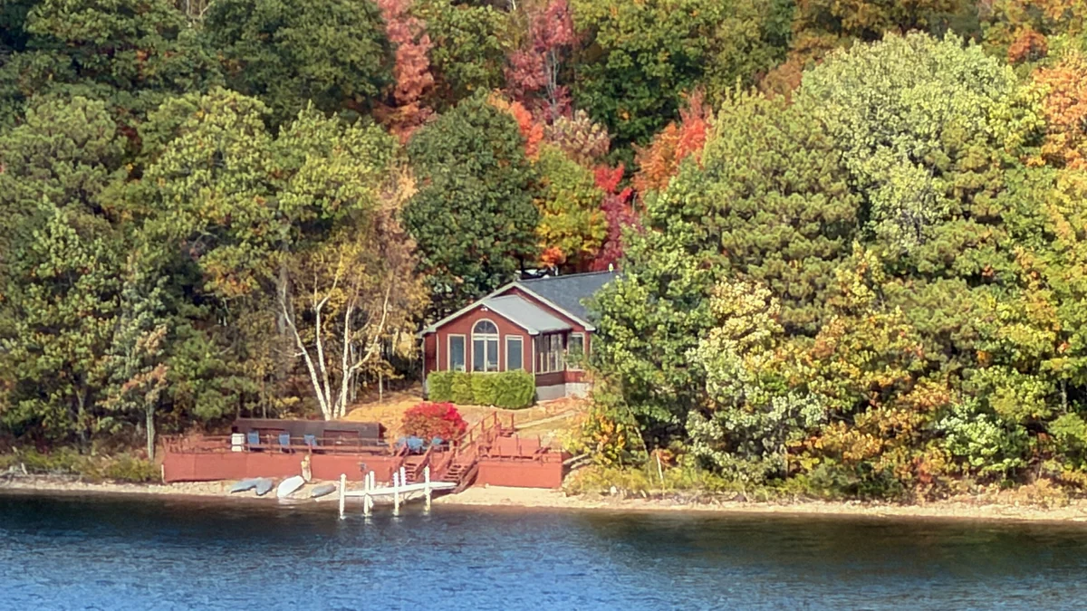 The Loon Hollow home, dock and autumn trees across foreground lake water